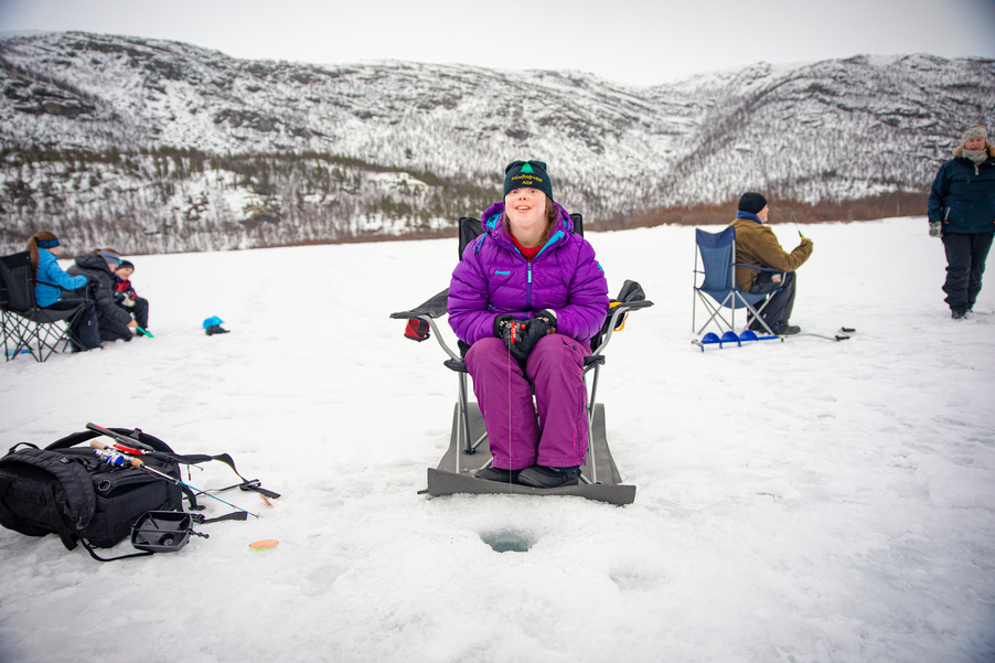 Foto: Beyond Horizons En flicka med downs syndrom sitter och pimplar på en is. I bakgrunden syns snöiga berg.